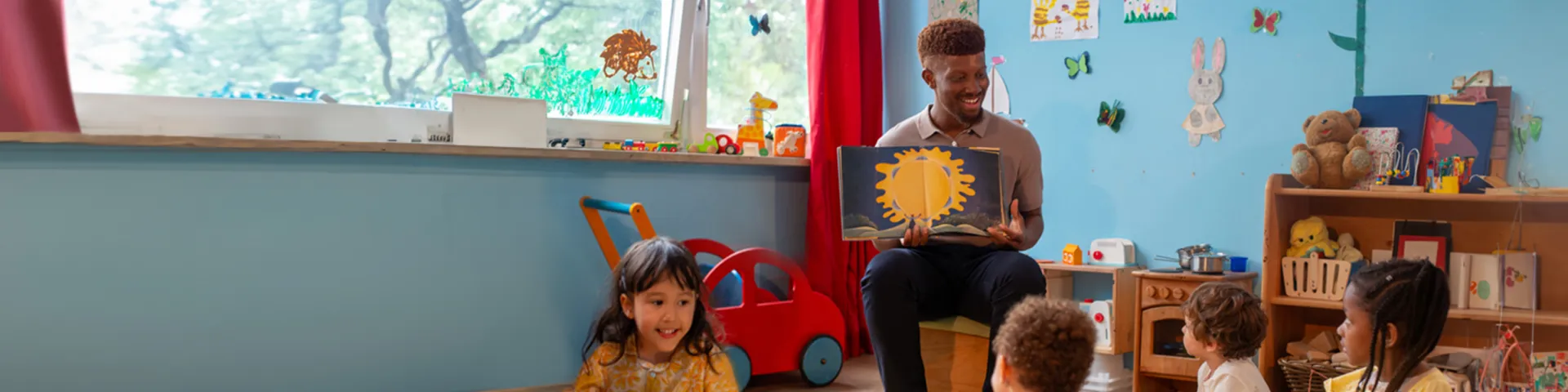 A male teacher reading stories from a book in kindergarten kids.