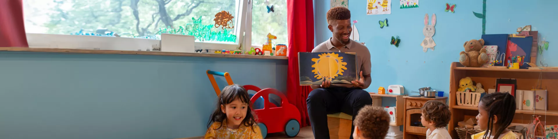 A male teacher reading stories from a book in kindergarten kids.