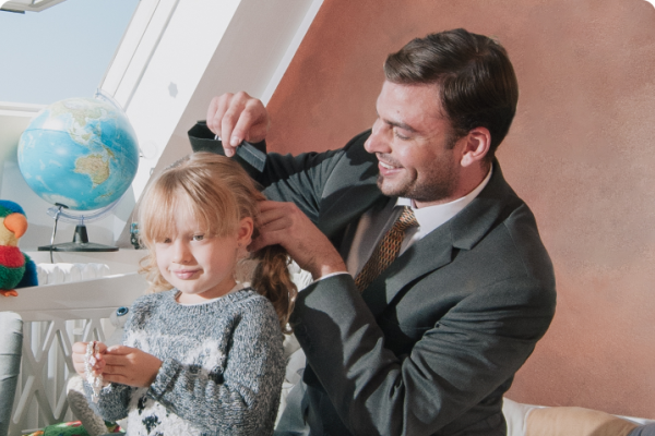 A working father dressed in a suit combing and styling the hair of his daughter 
