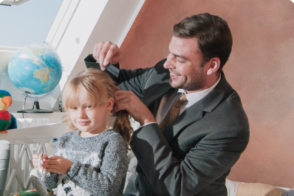 A working father dressed in a suit combing and styling the hair of his daughter